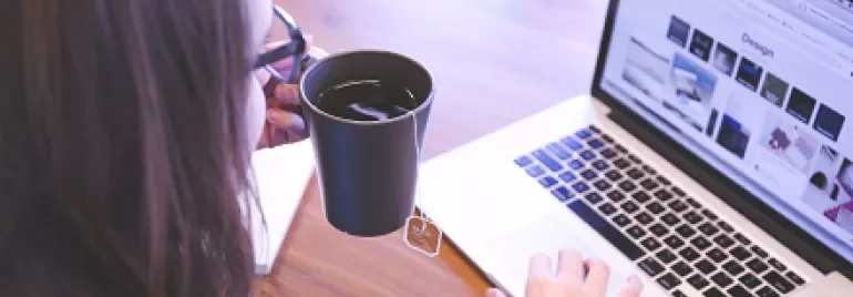 Persona beve tè mentre usa il portatile su un tavolo di legno.