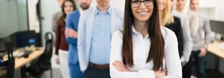 Gruppo di persone in ufficio, persona in primo piano con occhiali sorridente.