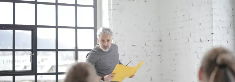 Persona con cartellina gialla parla a due persone in ufficio.