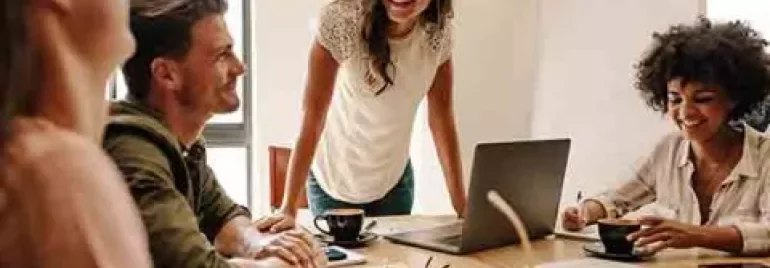 Persone in riunione sorridenti intorno a un tavolo con laptop.