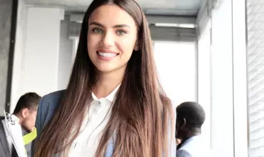 Persona sorridente con capelli lunghi, in un ufficio.