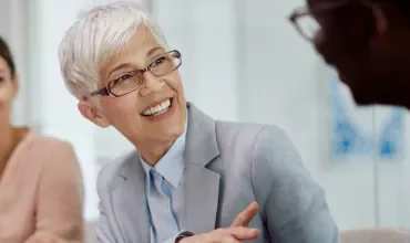 Persona sorridente in un meeting, indossa occhiali e abito formale.