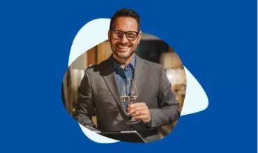 A smiling man holding a glass of wine on a blue background