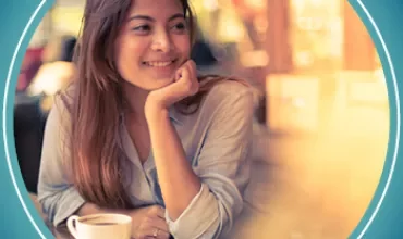 Persona sorridente seduta al tavolo di un bar con una tazza di caffè.