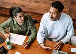 2 coworkers on a table talking while taking a coffee