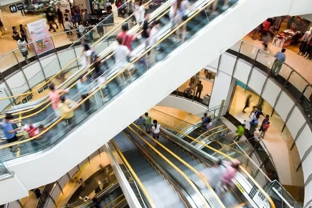 Centro commerciale affollato con scale mobili in movimento.