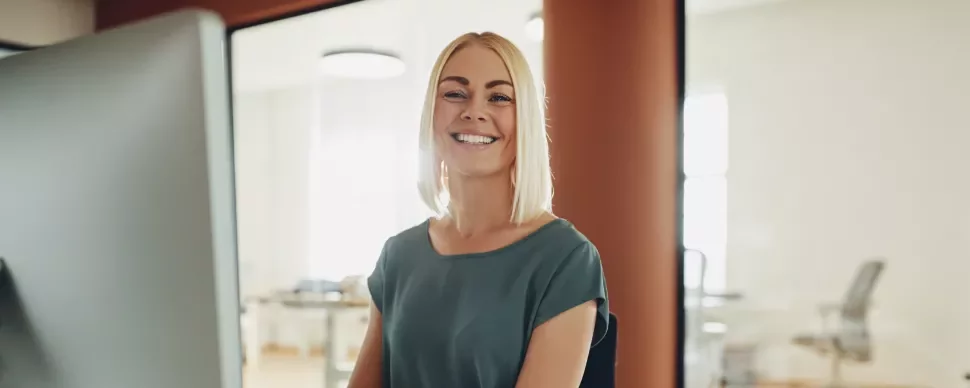 Persona sorridente seduta davanti a un computer in ufficio illuminato.