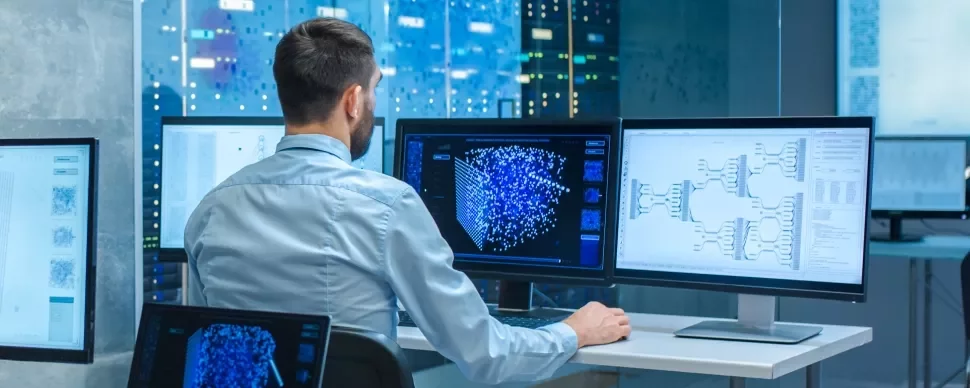 Persona al computer analizza dati su più schermi.