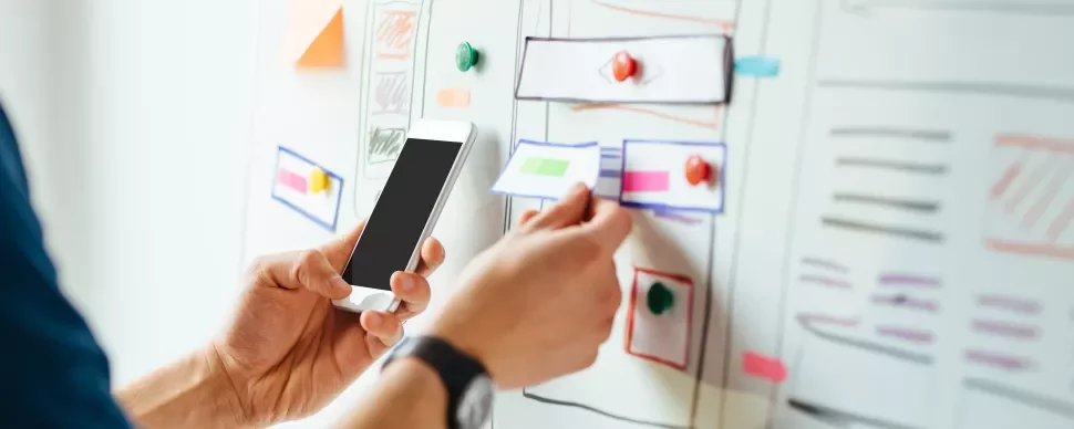 Persona che utilizza uno smartphone e osserva un progetto su lavagna