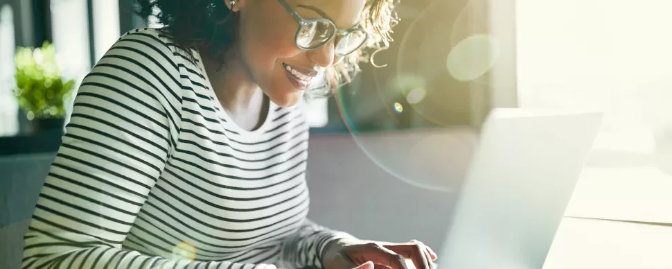 Persona sorridente che utilizza un laptop, con luce solare che entra dalla finestra.