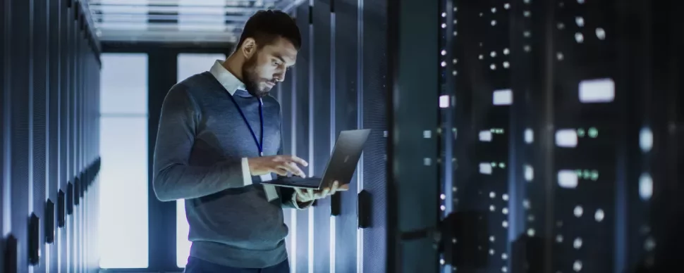 Persona controlla i dati su un laptop in una stanza server.