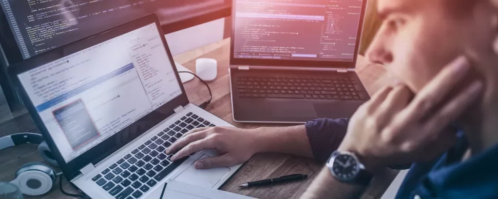 Persona al lavoro su più laptop con codice sullo schermo.