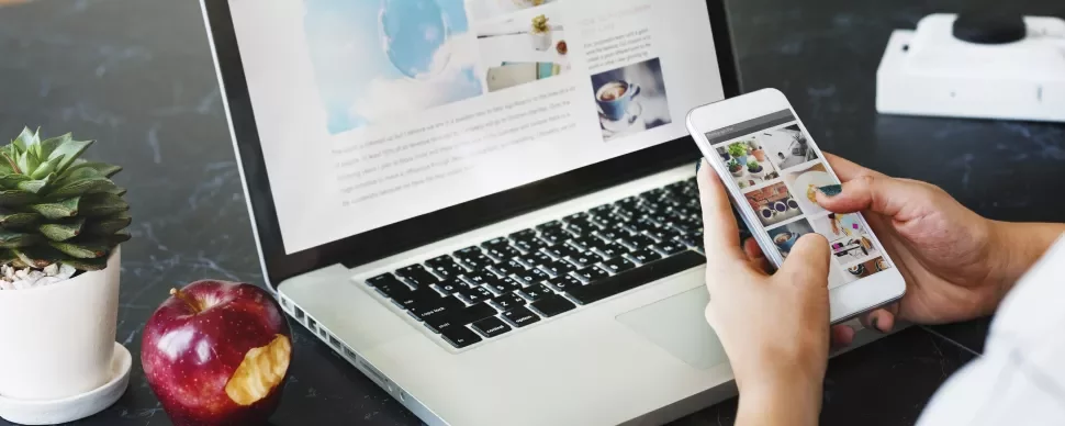 Persona che usa smartphone e laptop, con una mela e una pianta a lato.