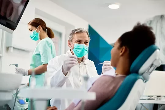 Dentista con maschera e paziente in studio odontoiatrico.
