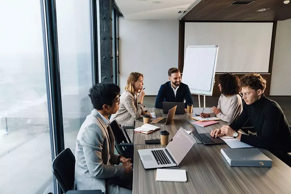 Riunione d'ufficio in corso attorno a un tavolo con laptop.