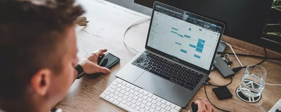 Persona al lavoro su laptop con calendario aperto.