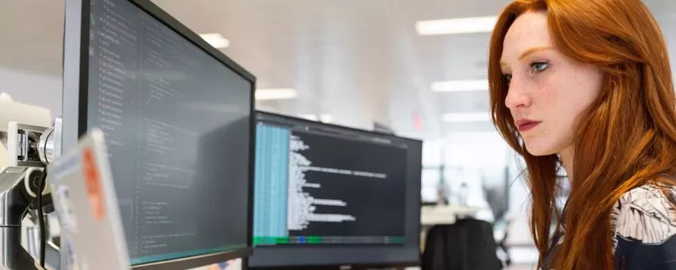 Persona che lavora al computer con codice su due monitor.