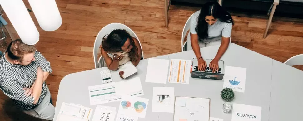 Persone al lavoro in un ufficio con documenti e laptop su un tavolo.