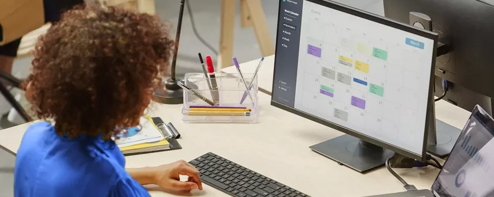 Persona in ufficio al computer controlla un calendario digitale.