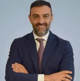 Persona in abito blu con braccia incrociate su sfondo neutro.