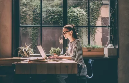 Persona al computer vicino a una finestra con piante.