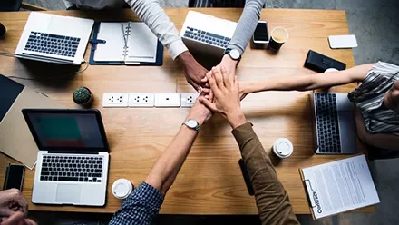 Persone riunite intorno a un tavolo con computer portatili.