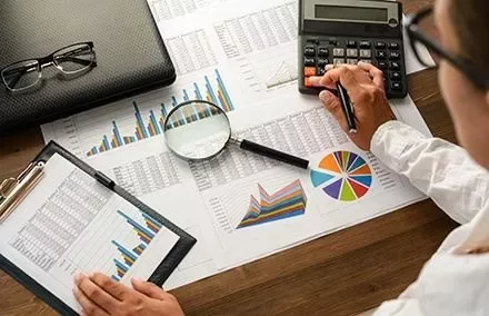 Persona al lavoro con grafici e calcolatrice su una scrivania.