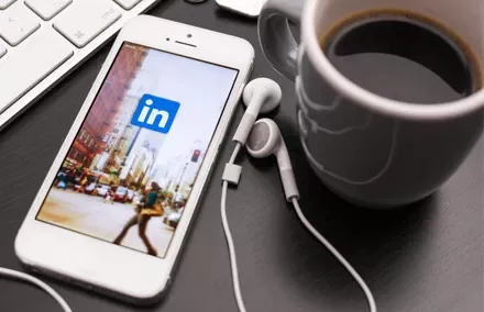 Smartphone con app LinkedIn aperta su scrivania accanto a tazza di caffè.