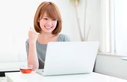 Persona sorridente davanti a un laptop con una tazza di tè sul tavolo.