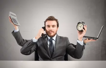 Persona multitasking con telefono, sveglia, calcolatrice e laptop.