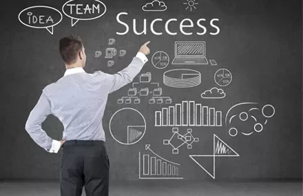 Persona davanti a una lavagna con disegni di grafici e la parola 'Success'.