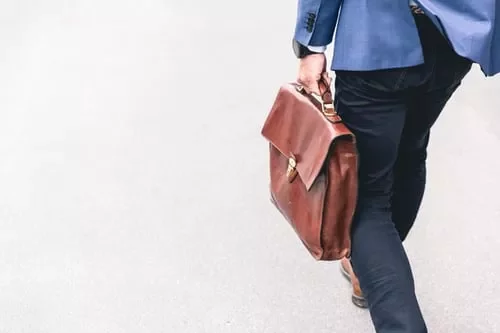 Persona che cammina con una borsa di pelle marrone.