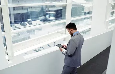 Persona in abito grigio guarda un tablet vicino alla finestra.