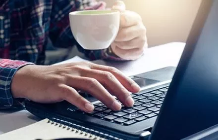 Persona al lavoro su un laptop tenendo una tazza da caffè.