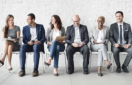 Gruppo di persone sedute in attesa, indossano abiti formali.