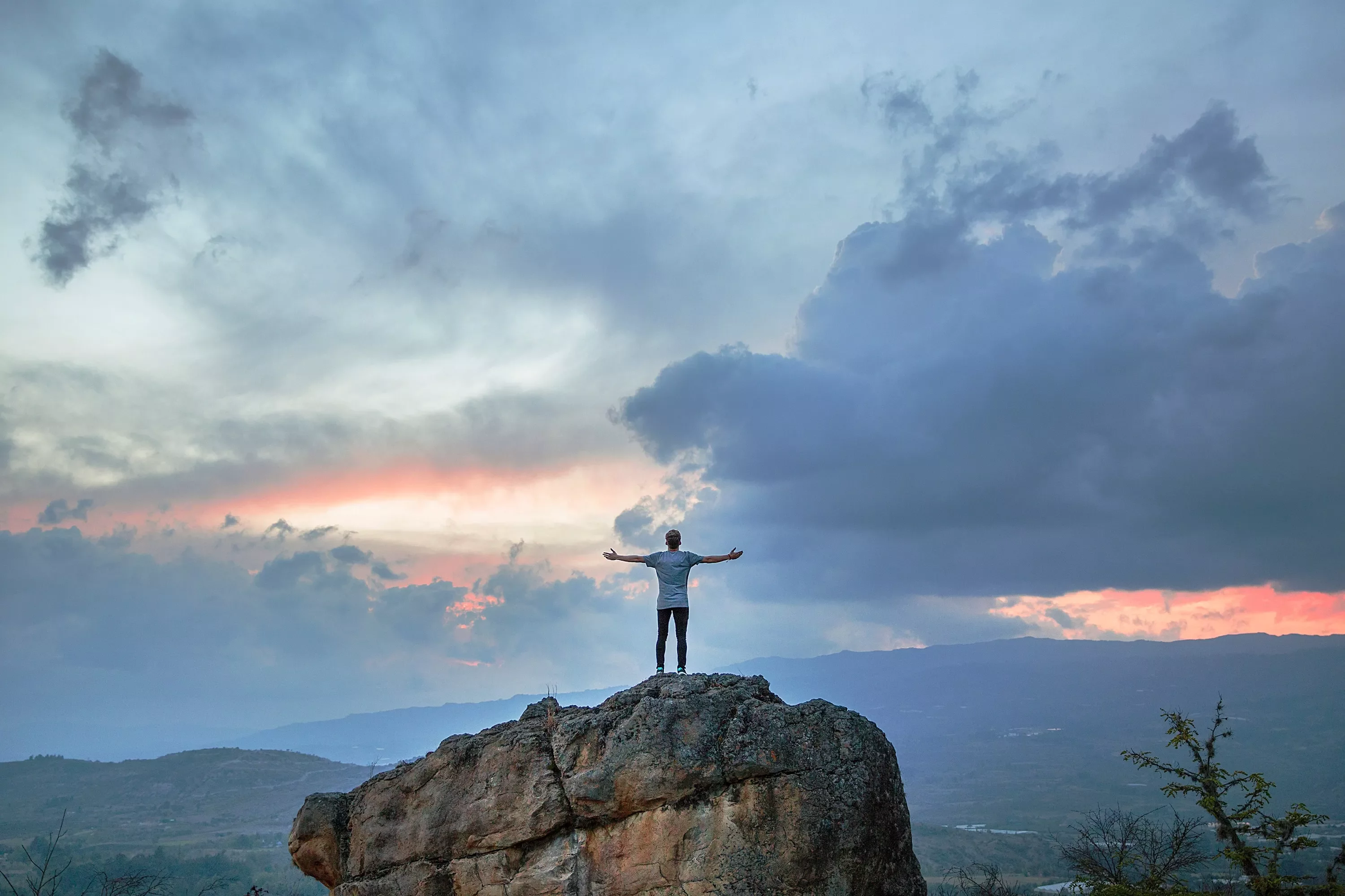 Persona su una roccia con le braccia aperte verso il cielo al tramonto.