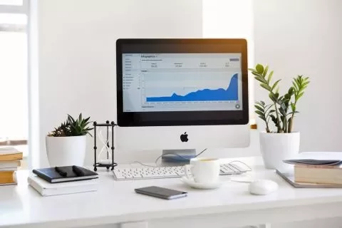 Scrivania con computer e grafico a schermo, piante e tazza di caffè.