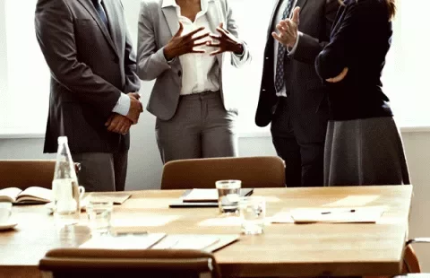 Persone in abiti formali discutono davanti a un tavolo da riunione.
