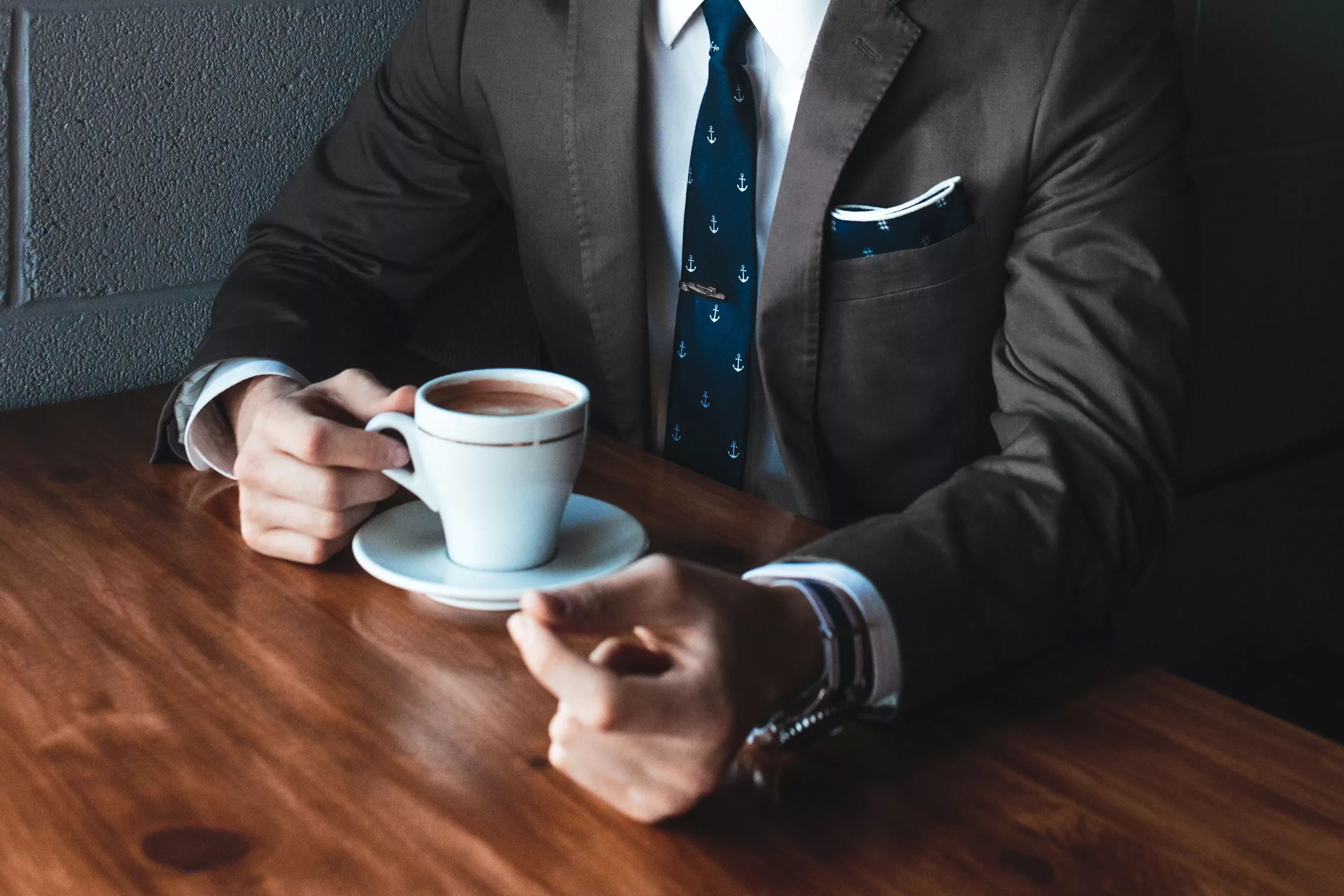 Persona in abito tiene una tazza di caffè su tavolo di legno.