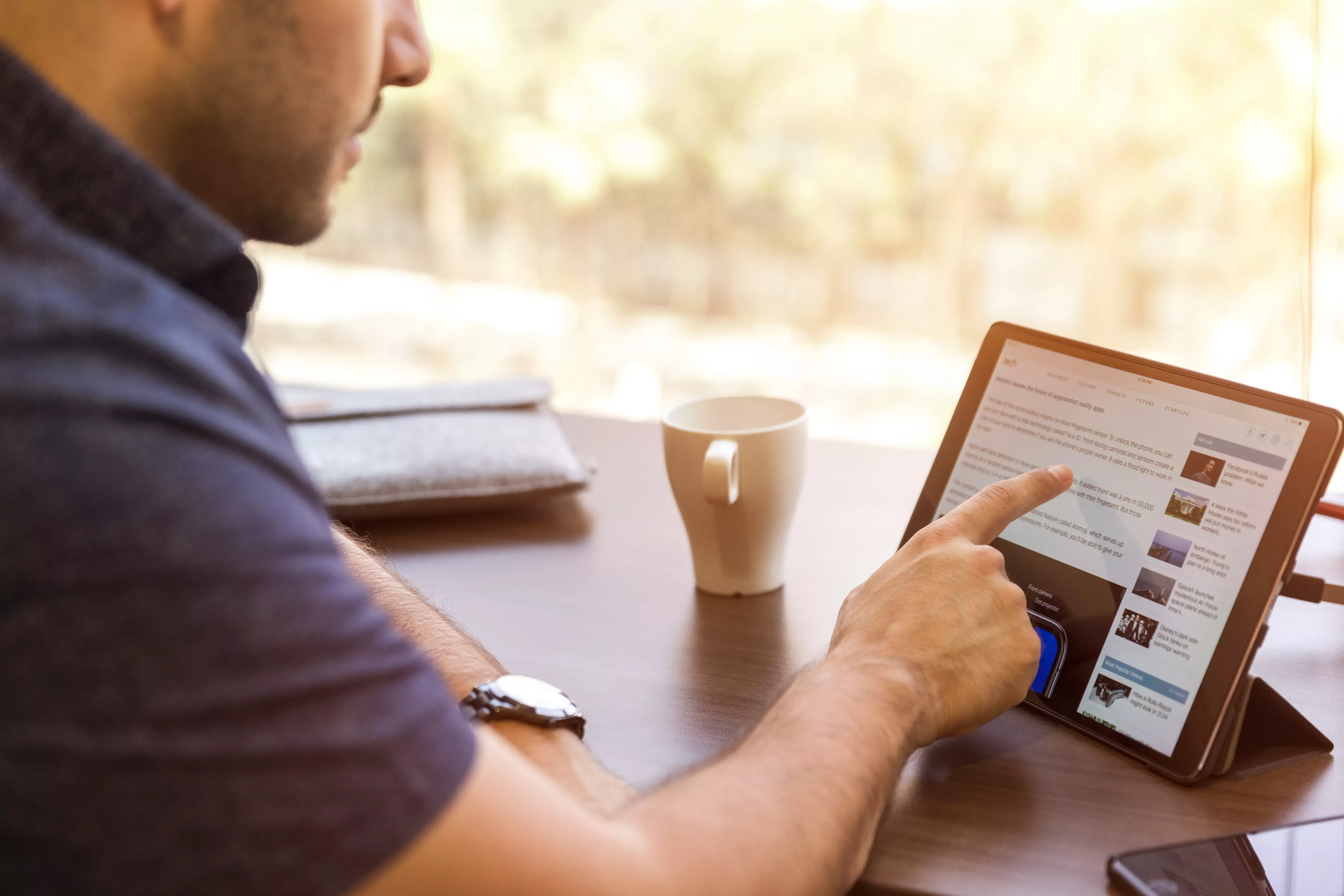 Persona che usa un tablet al tavolo con tazza di caffè.