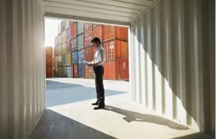 Persona in piedi vicino a container colorati, con documenti in mano.