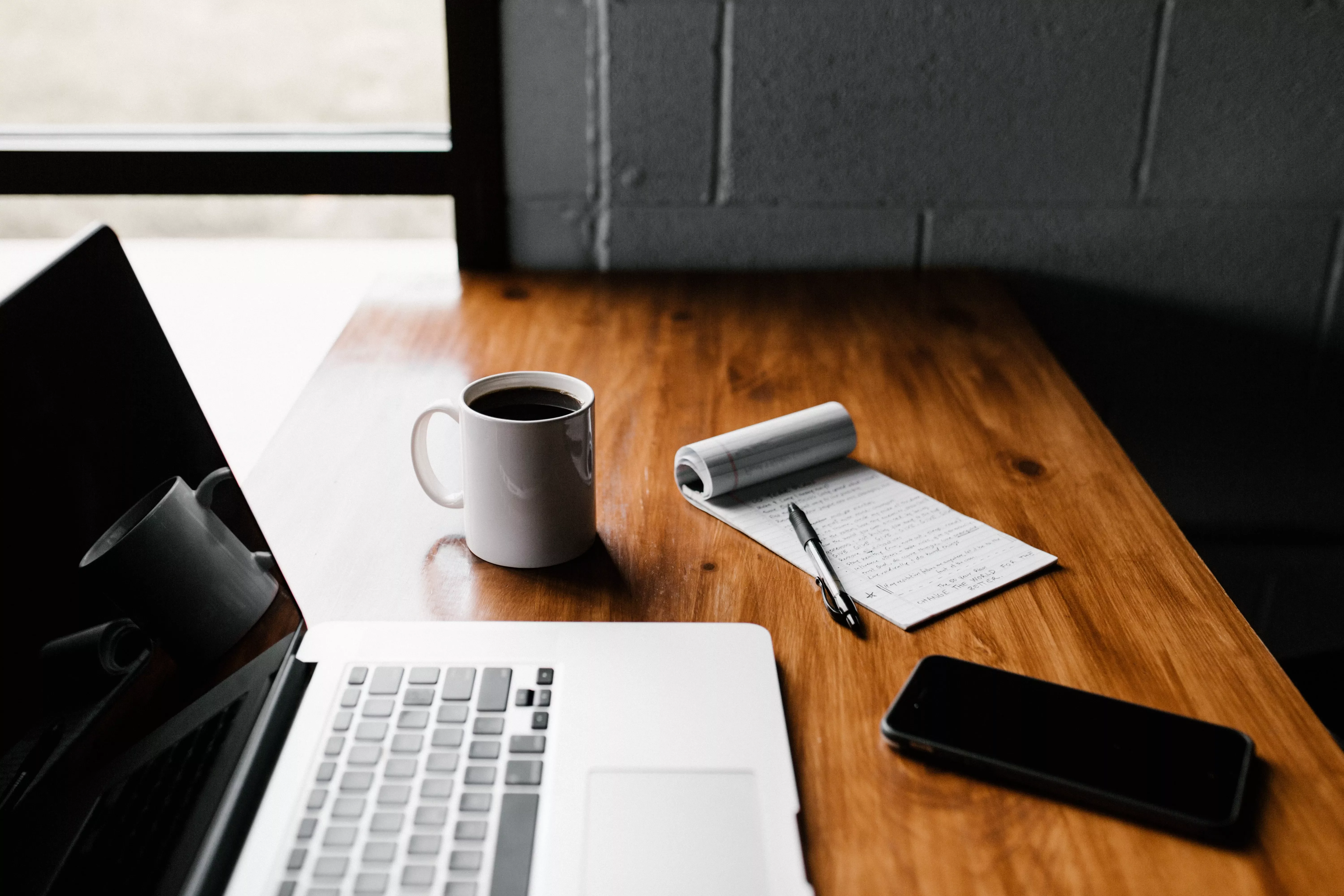 Scrivania con laptop, tazza di caffè, taccuino e penna.