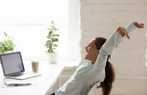 Persona felice si allunga alla scrivania accanto a un laptop.
