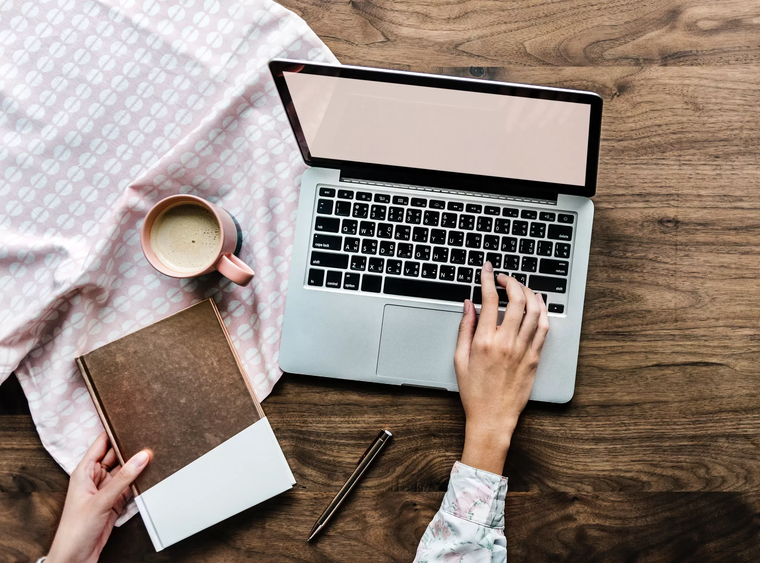 Persona usa un laptop con una tazza di caffè e un libro su tavolo di legno.